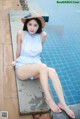 A woman in a blue dress and straw hat sitting by a swimming pool.