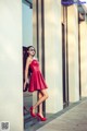 A woman in a red dress leaning against a wall.