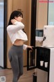 A woman in a white shirt and gray leggings standing next to a water dispenser.