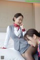 A woman in a gray suit sitting on a bed next to another woman.