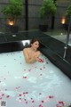 A woman in a bathtub with rose petals floating in it.