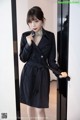 a woman in a black trench coat standing in front of a mirror