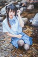 A woman in a blue shirt and skirt sitting in a stream.