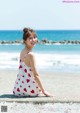 A woman sitting on the edge of a concrete wall by the ocean.