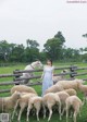 A woman standing in front of a herd of sheep.