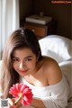 A woman laying on a bed holding a pink flower.