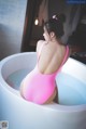 A woman in a pink bathing suit sitting in a bathtub.