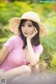 A woman in a pink shirt and a straw hat sitting in the grass.